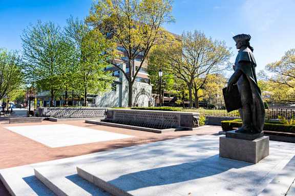A statue of a person stands on a pedestal in a park.