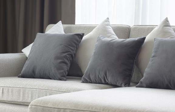 A grey couch with a pillow and a small table with a plant and a picture frame.