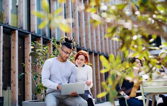 A man and a woman are sitting on a bench with a laptop.