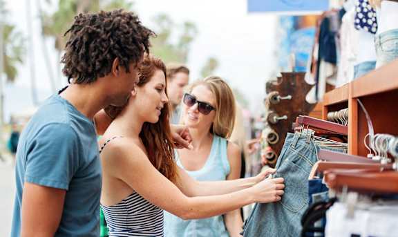 A woman is holding a denim jacket while standing next to a man and a woman in a clothing store. at The Aster, California, 90024