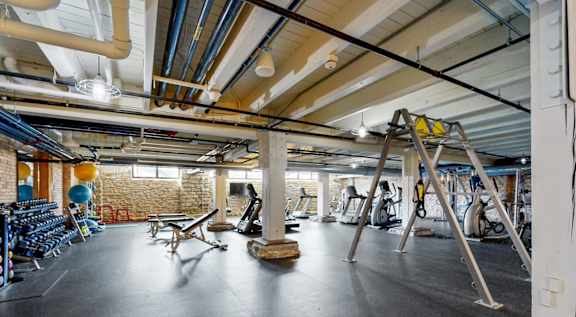 A gym with a variety of exercise equipment and a brick wall in the background.