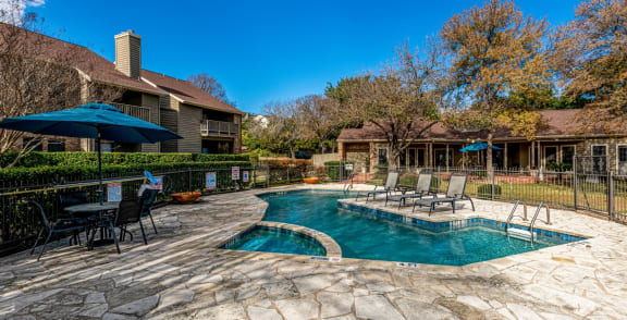 a swimming pool with chairs and umbrellas in front of a house