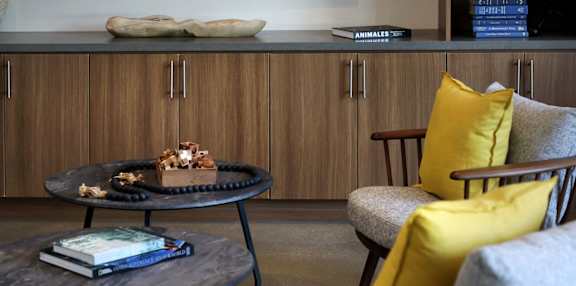 A living room with a grey armchair, a round table with a book and a cake on it, and a bookshelf with a sign that says "ANIMALS".