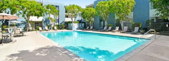 a swimming pool in front of a building with chairs and trees