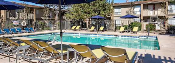 A pool with yellow chairs and blue umbrellas.
