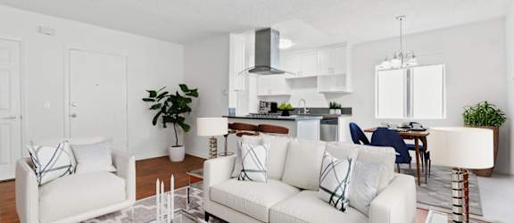 A modern living room with white furniture and a kitchen in the background.