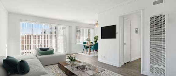 A white couch with green pillows sits in a room with a coffee table in front of it.