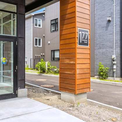 The image shows a modern building with a glass door and a wooden column with the number 177 on it.