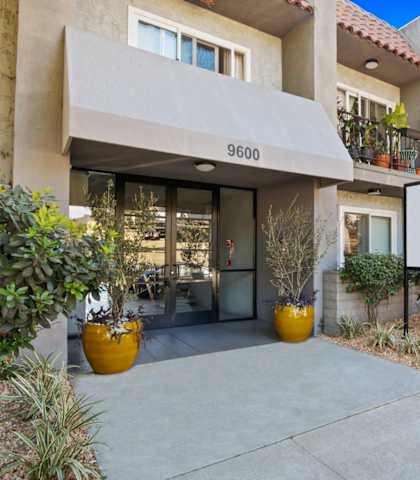 the sidewalk in front of a building with a patio and potted plants