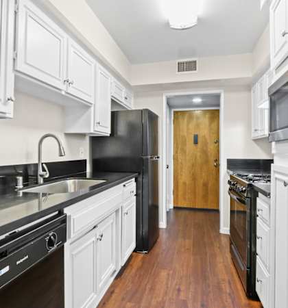a kitchen with white cabinets and black appliances and a door to a hallway