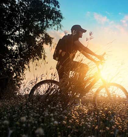 a man riding a bike in a field with the sun behind him