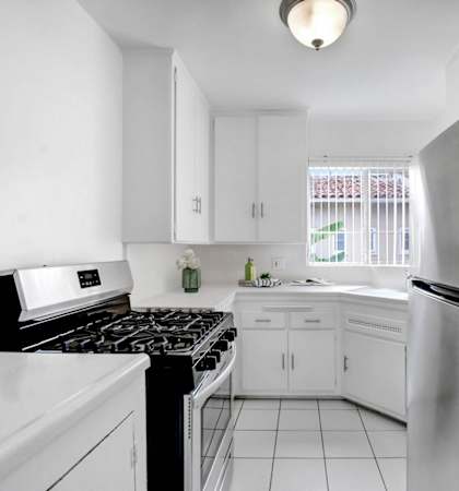 A black refrigerator stands in a kitchen with white cabinets and appliances.