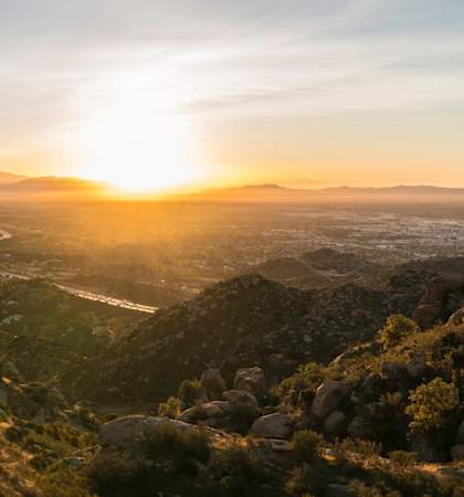 A sunrise over a valley with a river and mountains in the distance.