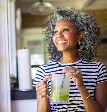 A woman with curly hair is holding a glass with a green drink in it.