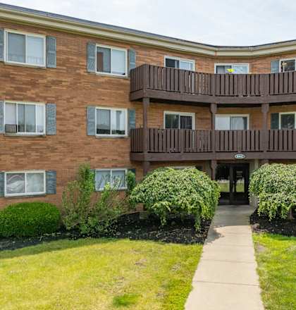 A brown building with a balcony and bushes in front.