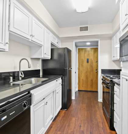 a kitchen with white cabinets and black appliances and a door to a hallway