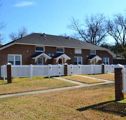 A white picket fence surrounds a brick house.