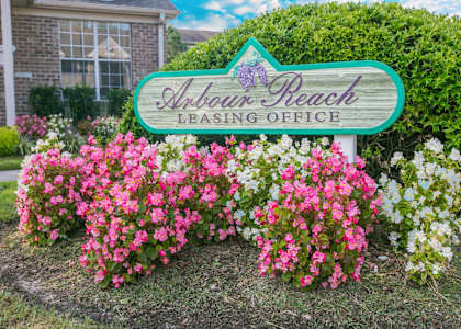 A sign for a leasing office is surrounded by flowers.