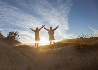 Two people standing on a hill with their arms raised in the air.