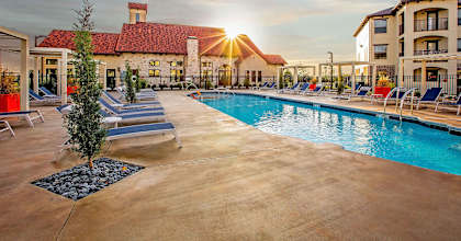 A sunset view of a pool area with lounge chairs and a building in the background.