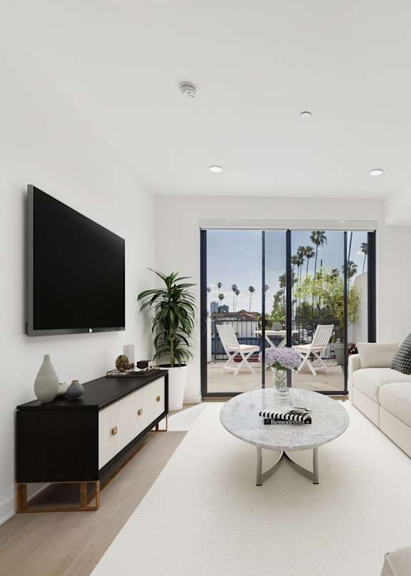 A living room with a grey couch, a wooden coffee table, and a large window with a view of palm trees.