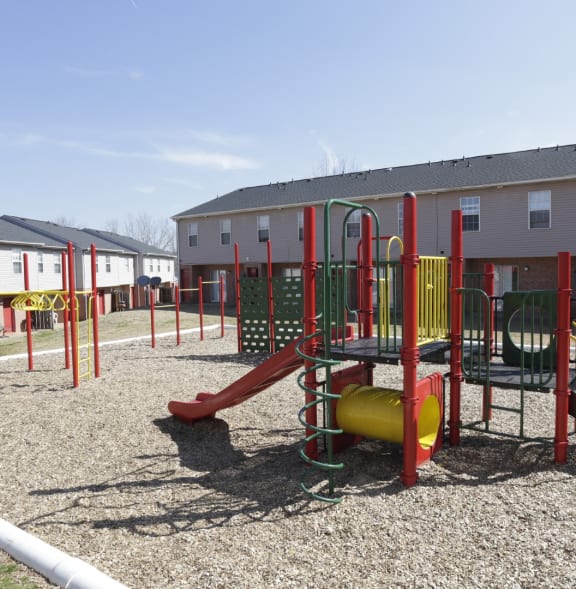A playground with a red slide and yellow and green swings.