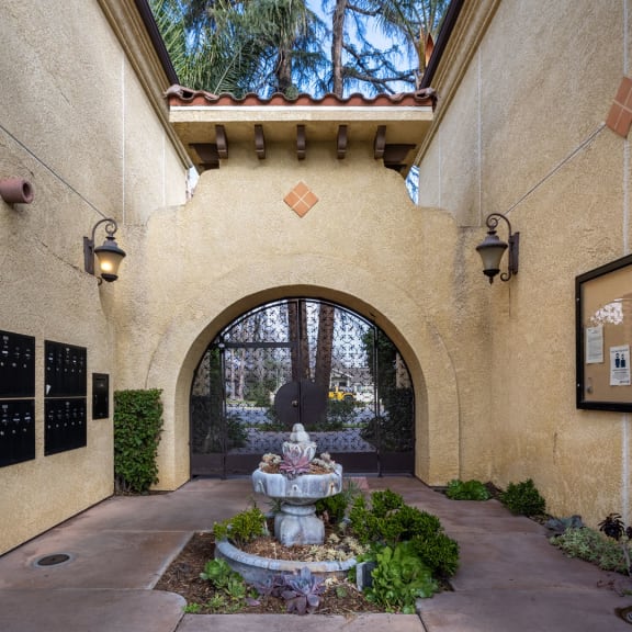 a fountain sits in the center of a courtyard in front of an archway at The Village Apartments, Van Nuys, California, 91406