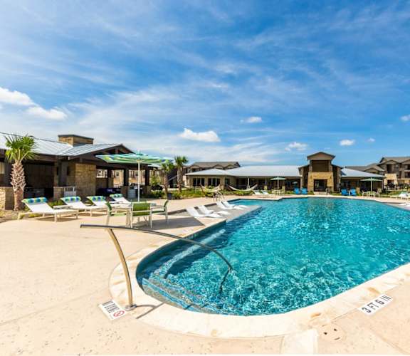 a large pool with lounge chairs and umbrellas in front of a building at Legacy Creekside Apartments, San Antonio, 78251