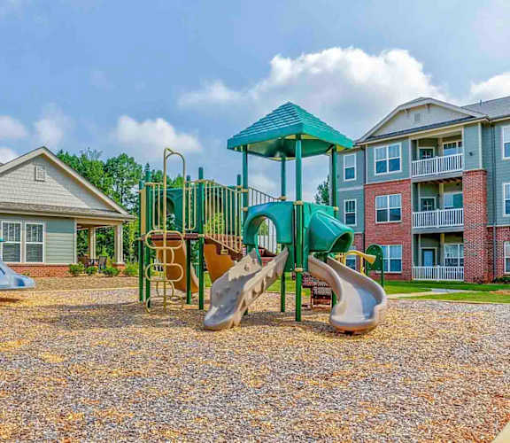 A playground with a green slide and a blue umbrella.