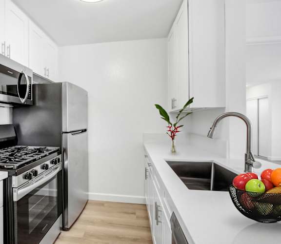 A modern kitchen with a stainless steel refrigerator, oven, and white cabinets.