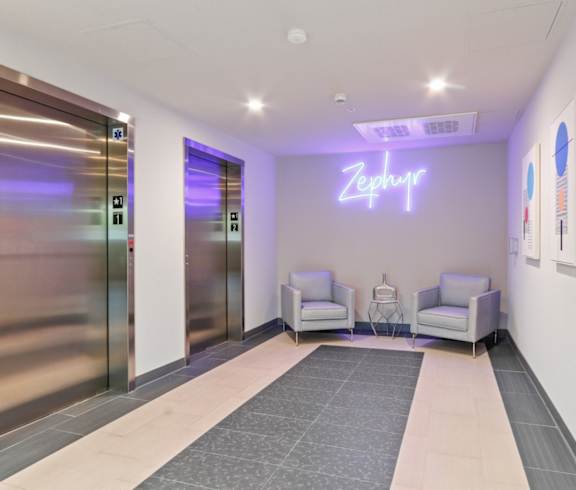 a lobby with elevators and chairs and a neon sign on the wall