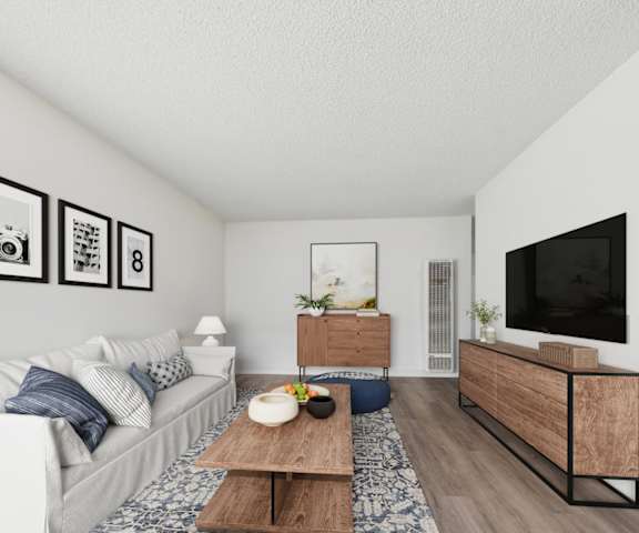 A living room with a white couch, a wooden coffee table, and a TV on the wall.