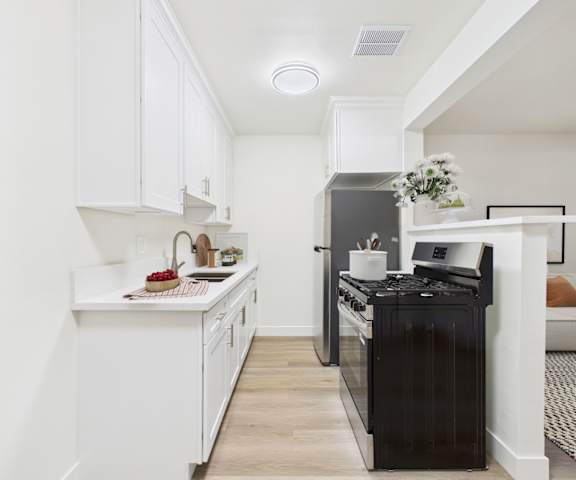 A black fridge sits in a white kitchen next to a white counter.