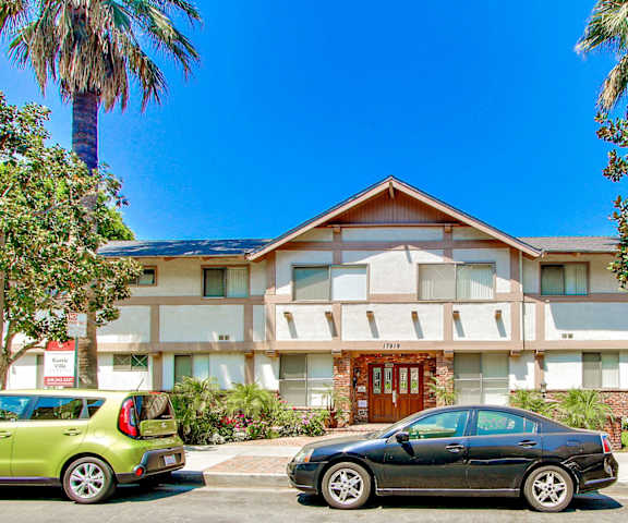 A black car is parked in front of a two-story building with a red door.