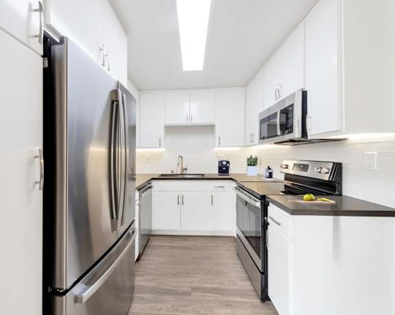 A modern kitchen with a stainless steel refrigerator and black countertops.