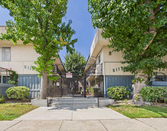 A white building with a black gate and a tree in front.
