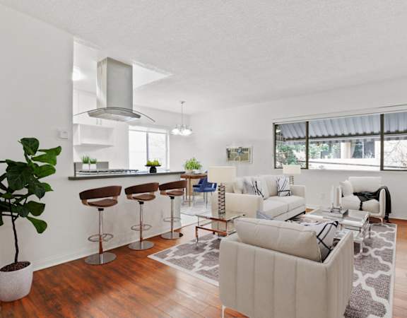 the living room and kitchen of an apartment with white couches and stools