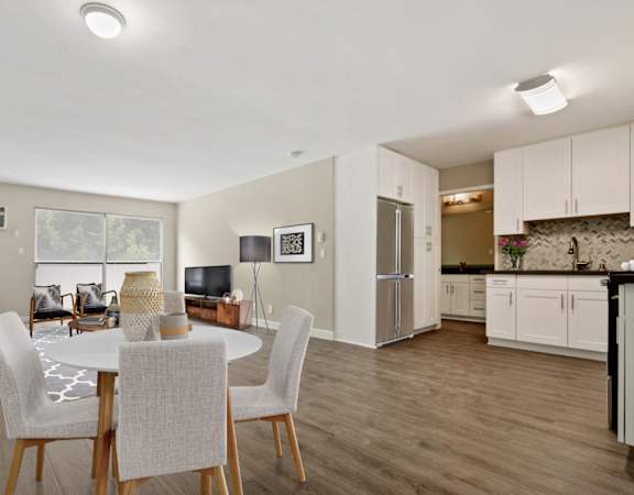 a living room with a white table and chairs and a kitchen with a stainless steel refrigerator and