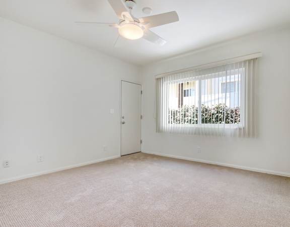 an empty living room with a window and a ceiling fan