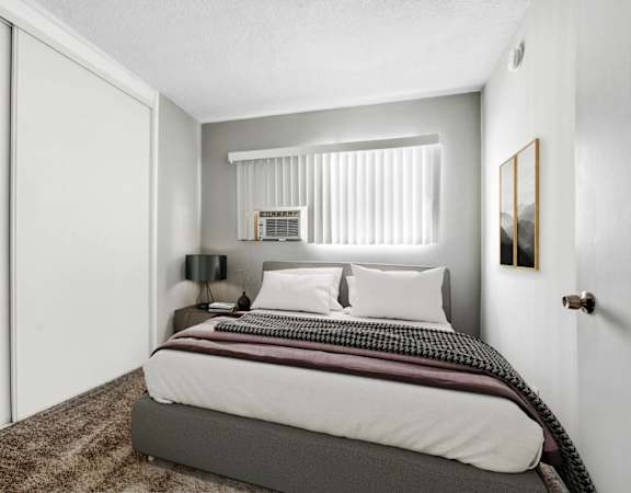 A bedroom with a bed, nightstand, lamp, and window.