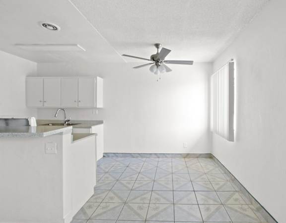 an empty kitchen with white cabinets and a ceiling fan
