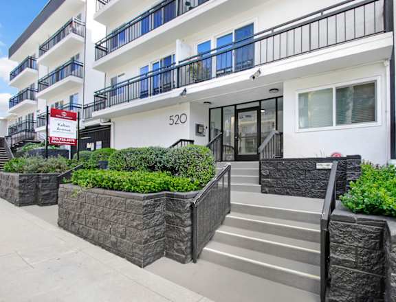 the front entrance of an apartment building with stairs and a sidewalk
