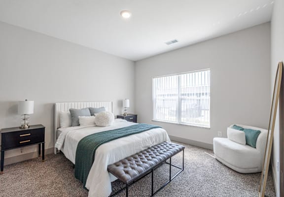 A bedroom with a bed, chair, and nightstand.