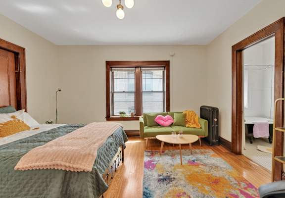 A bedroom with a bed, a green chair, and a window.