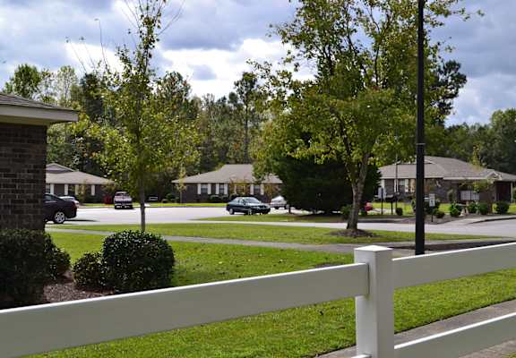 A white fence in front of a grassy area with houses and trees in the background.