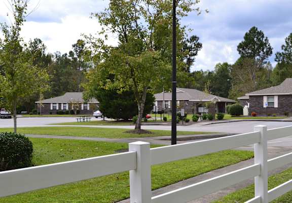A white fence in front of a grassy area with houses in the background.
