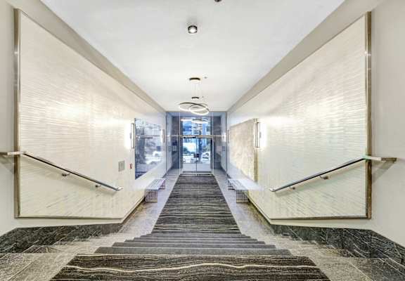 A long hallway with a carpeted staircase and a metal railing.