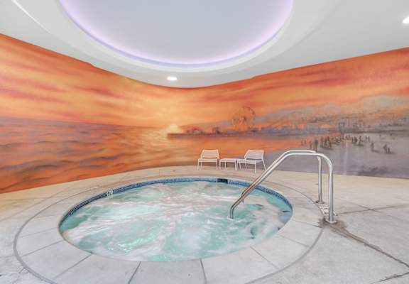 A hot tub in a room with a sunset mural on the wall.