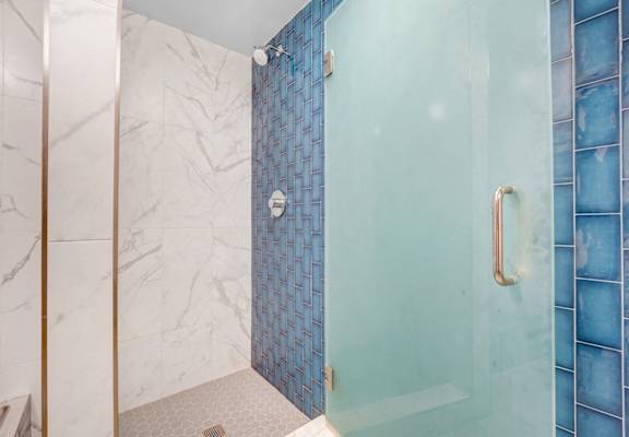 A shower area with a glass door and a marble wall.