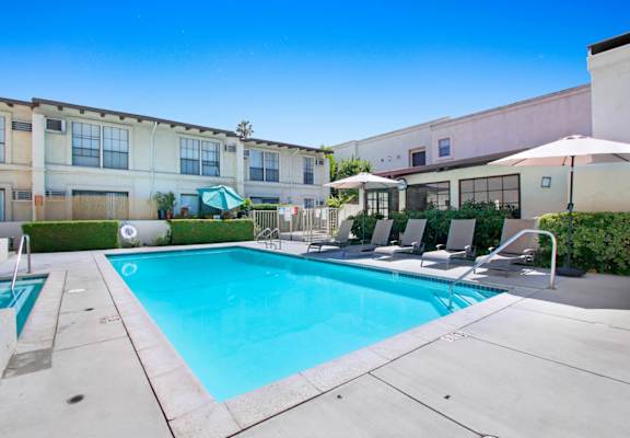 a swimming pool with lounge chairs and umbrellas in front of a building